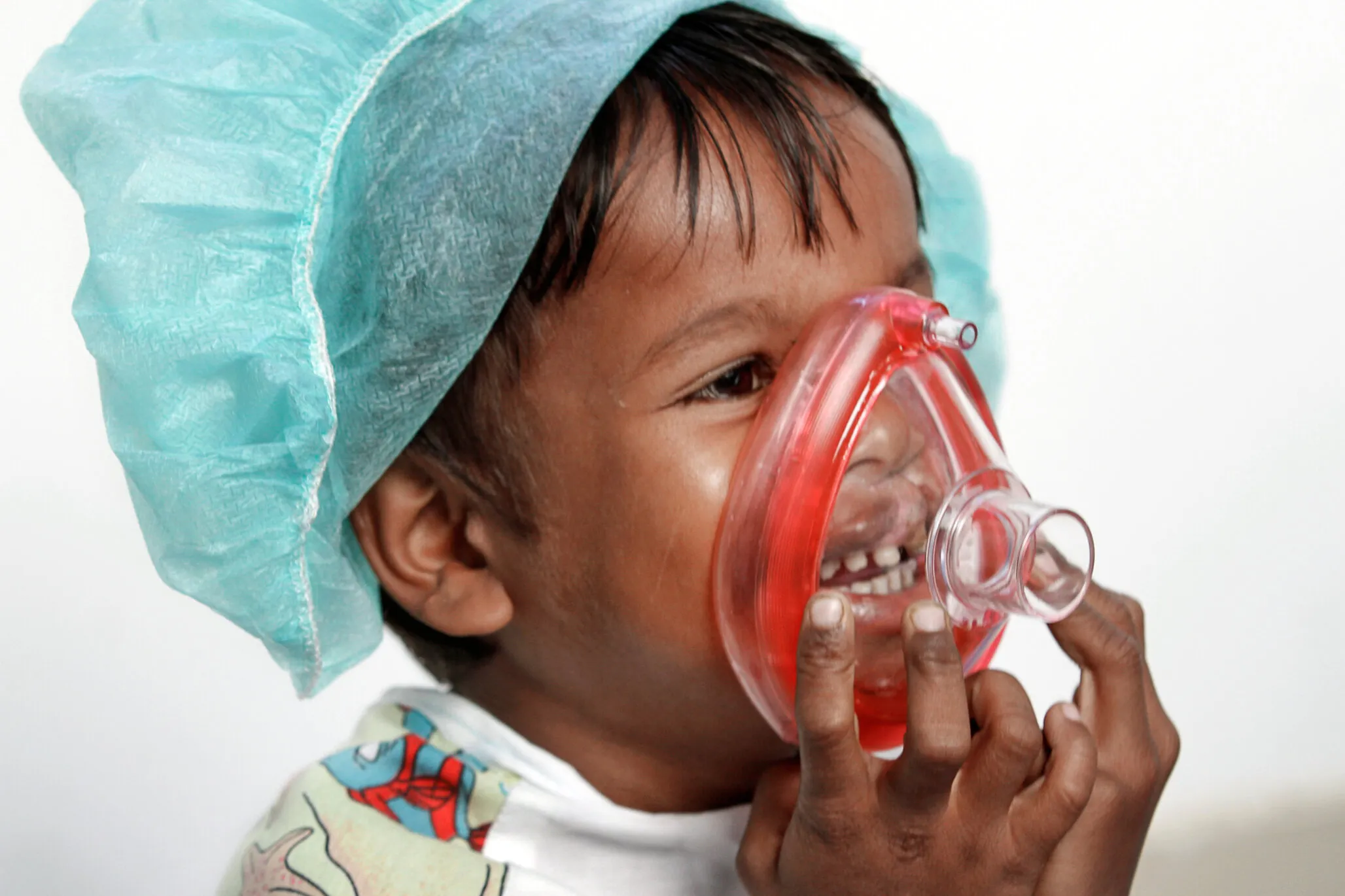 Sarban, 5 years old, wears a scrub cap and plays with a toy anesthesia mask over to help him become more comfortable with the medical equipment he will likely see after entering the operating room for his surgery