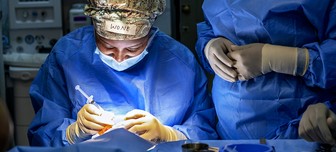 A spotlight shine on Dr. Wone Banda as she performs surgery. The nametag tapped to her surgical cap says "Wone" while another medical volunteer stands off to the right.