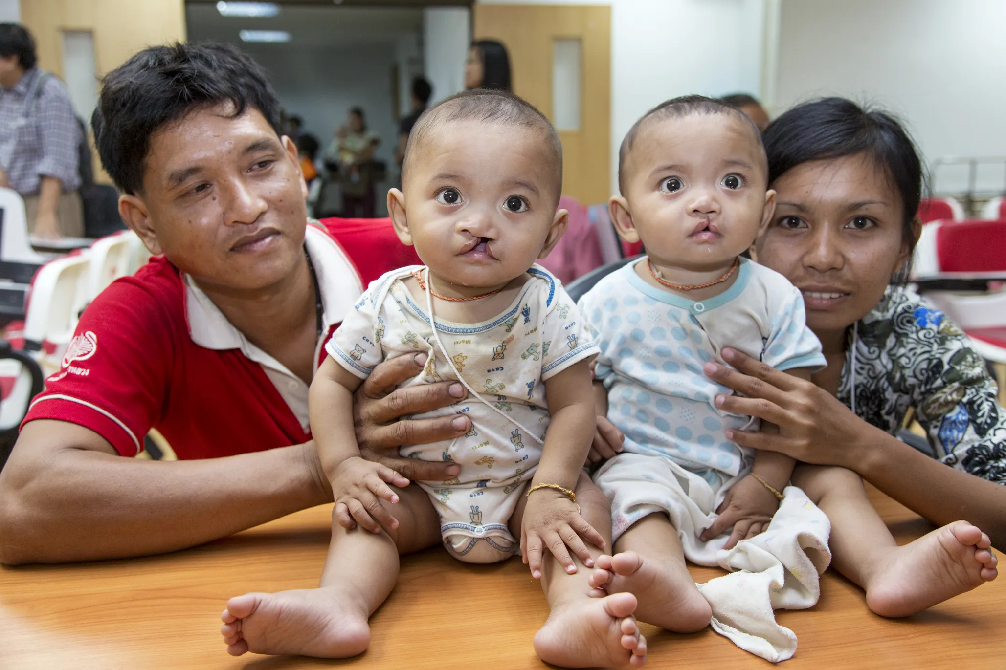 Manus, left, and Wanna hold their twin sons, Ou and Lak, right center, as they await their comprehensive health evaluations during an Operation Smile surgical program in Thailand.